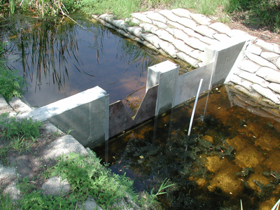 concrete wall spanning seepage channel with two stainless steel weir plates