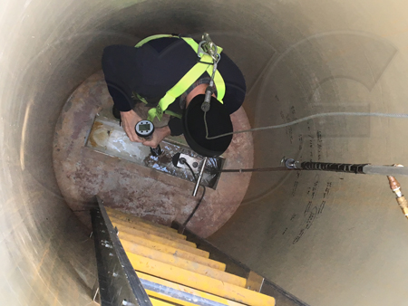 industrial operator checking flow velocity in a palmer-bowlus flume intergrated in a pretreatment monitoring manhole